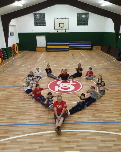 Děti a trenéři sedí ve tvaru srdce kolem loga Sokol na dřevěné podlaze tělocvičny